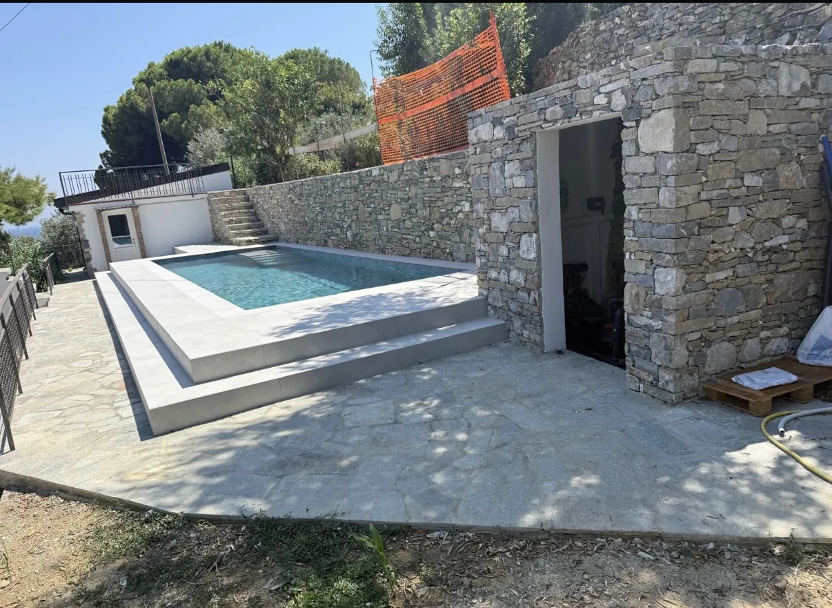 Piscina rialzata con pavimentazione in pietra e locale tecnico rivestito in pietra